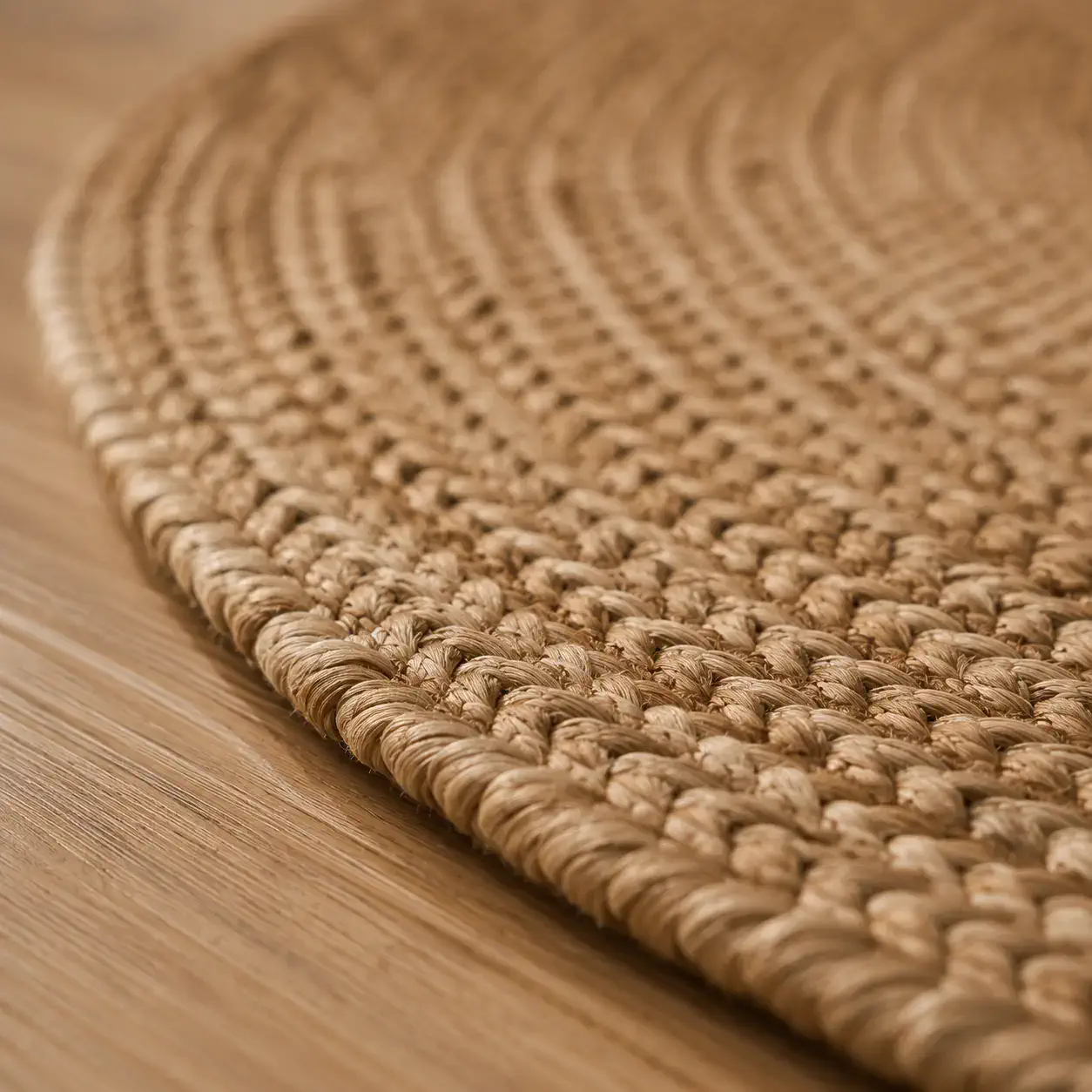 Close-up edge detail of the Daaira round braided jute rug showcasing handcrafted braid construction, natural jute fibres, and premium edge binding on warm oak flooring.