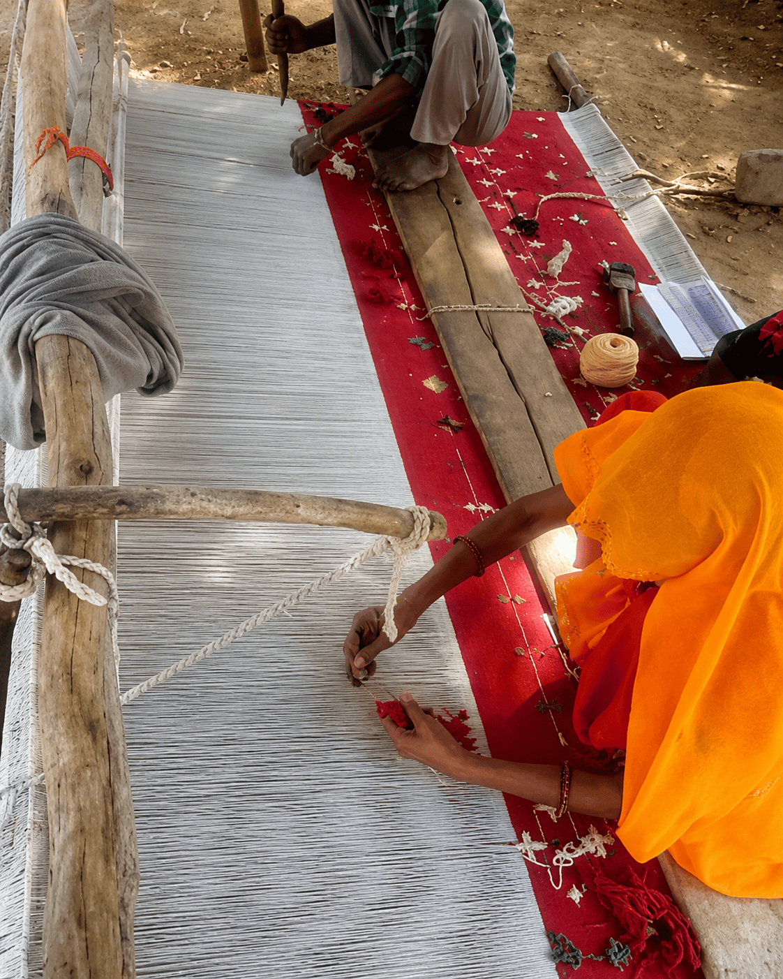 Artisan hand-knotting a wool rug on a floor loom at a Planet Arts workshop in Jaipur, India